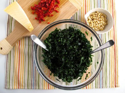Making Tuscan Kale Salad with parmesan, sundried tomatoes, and pine nuts.